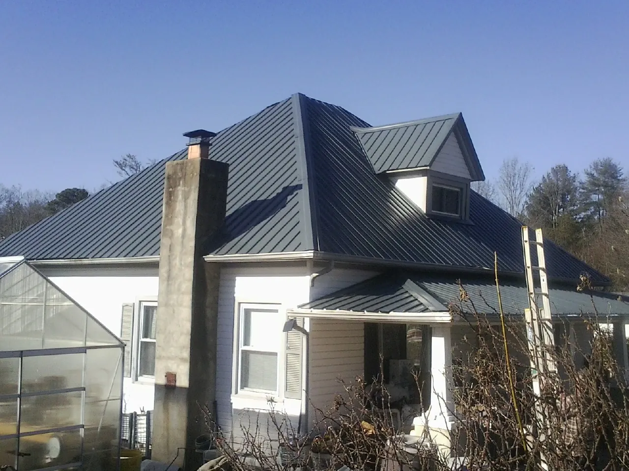 Dark blue standing seam metal roof on a white farmhouse with dormer — Slate & Tile Roof Repair by Roofing Brothers in Buchanan Dam