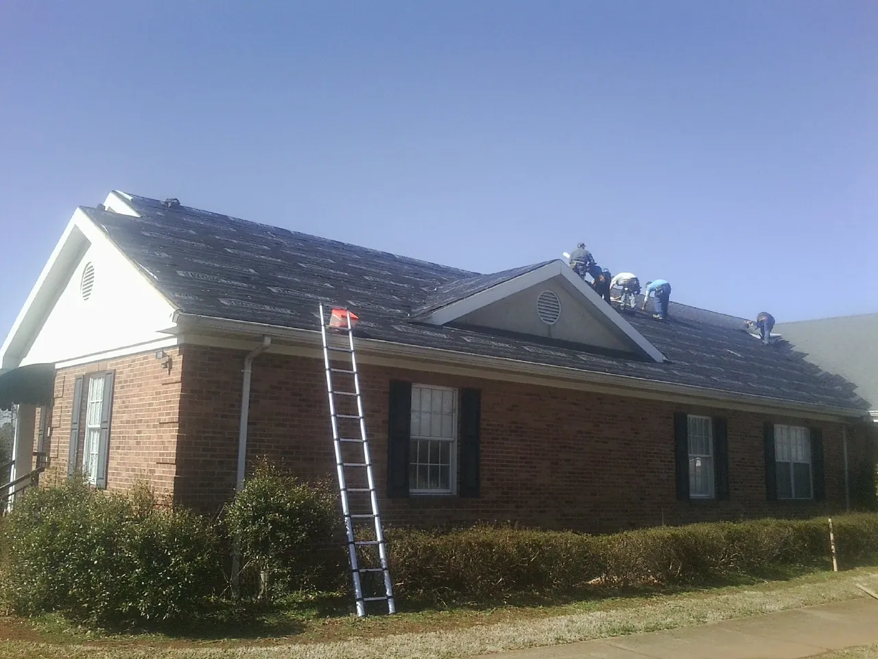 Crew tearing shingles off a brick ranch roof with a ladder set — Metal Roof Repair work by our crew in Buchanan Dam