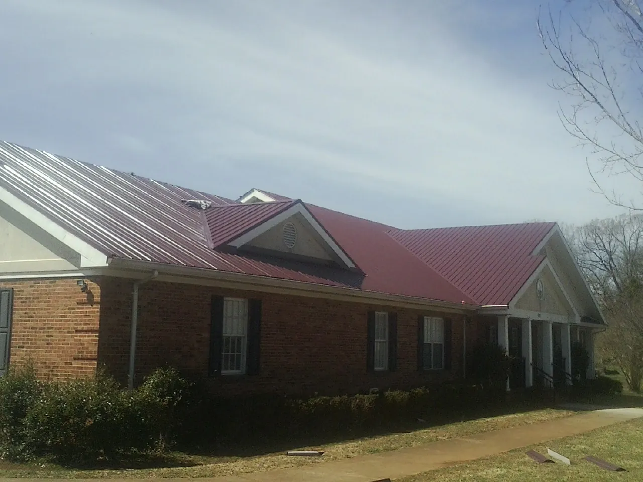 Red metal roof with gabled entries on a long brick building, from a Hail Damage Roof Repair job in Buchanan Dam