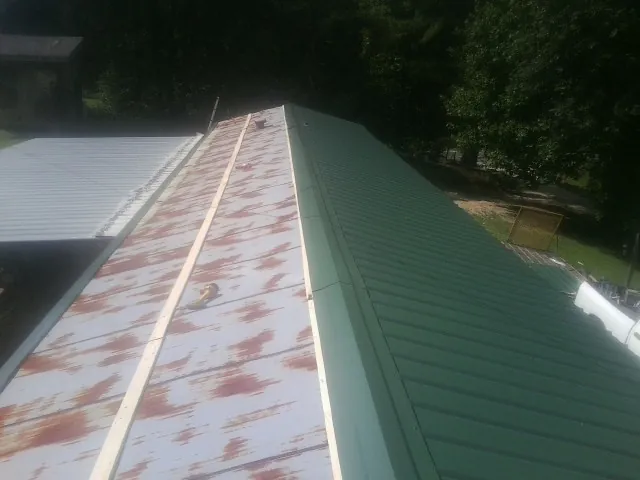 Old rusted panels beside newly installed green metal roofing — Wind Damage Roof Repair by Roofing Brothers in Buchanan Dam