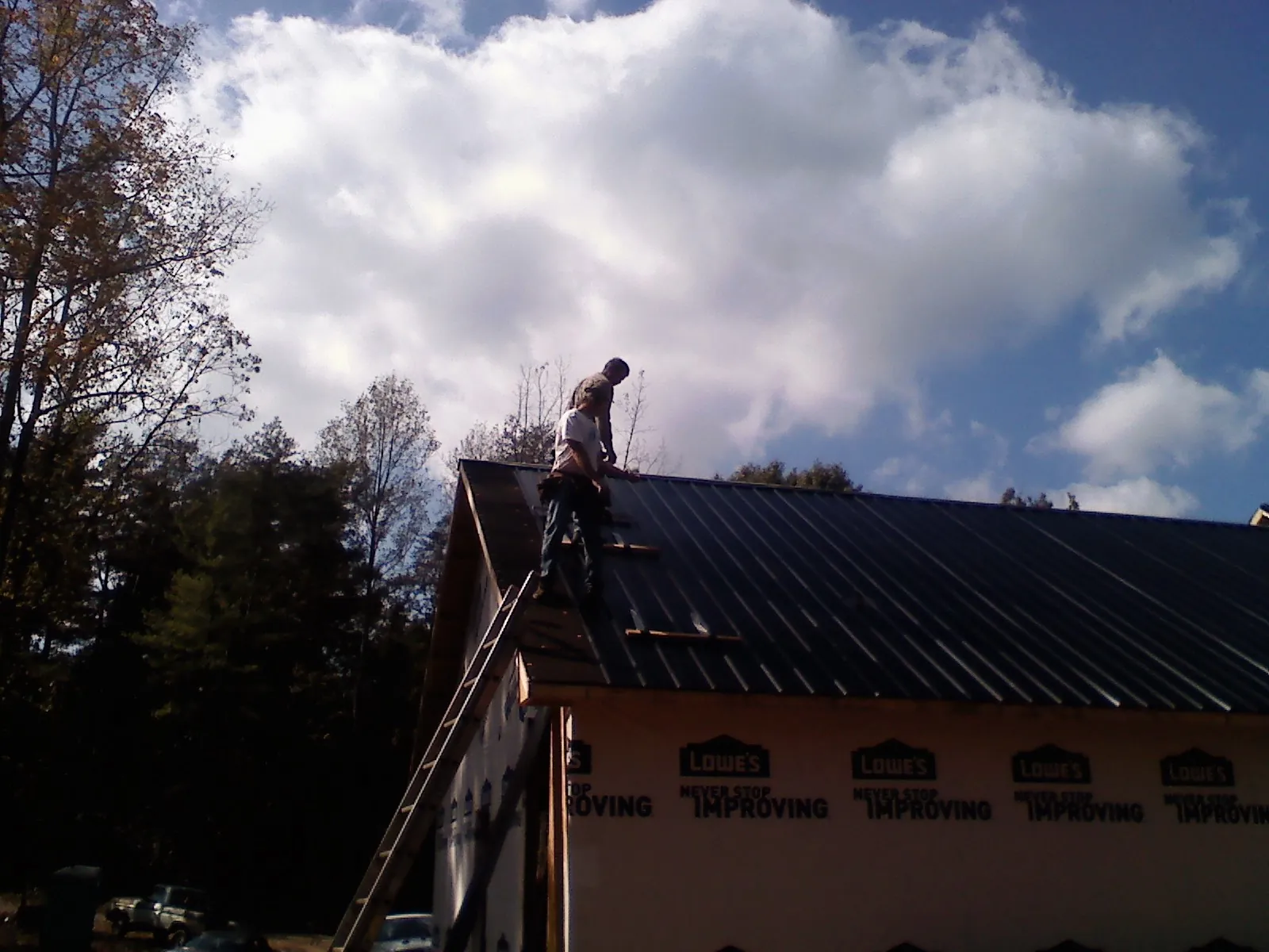 Roofer fastening dark metal panels high against a cloudy sky, from a Roof Inspection job in Buchanan Dam