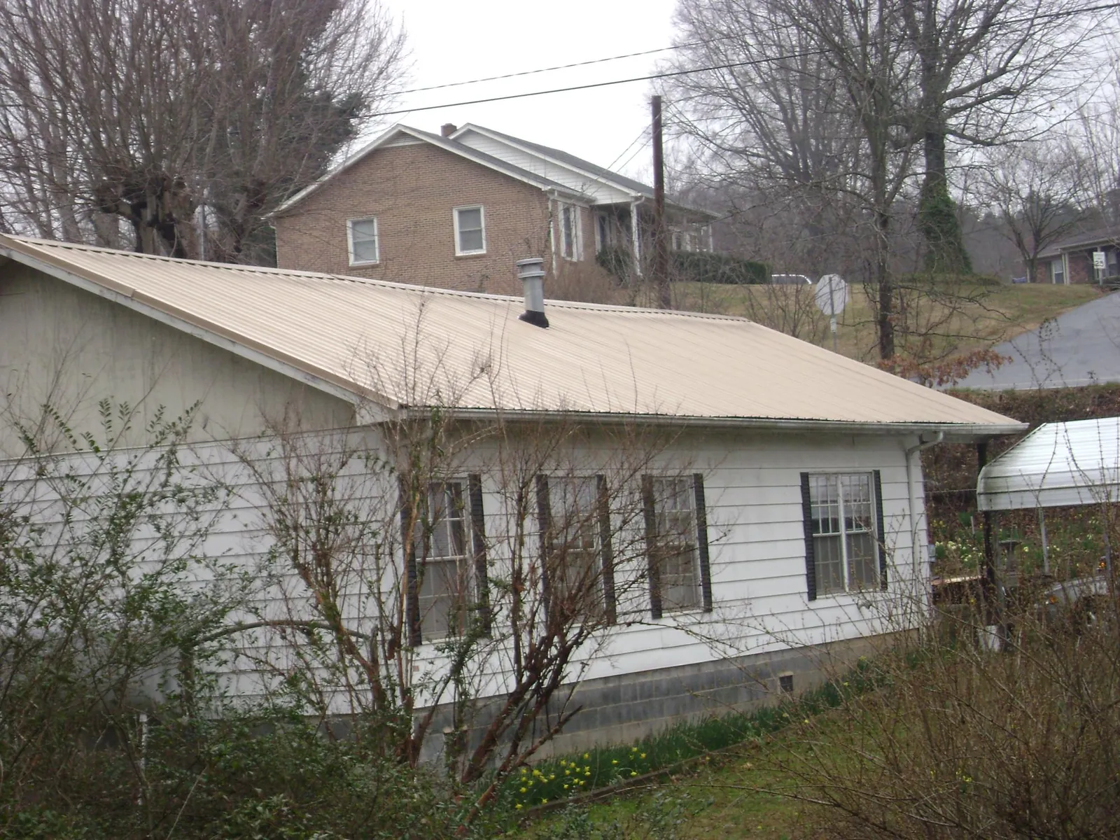 Tan metal roof on a white sided house set into a hillside — Commercial Roofing by Roofing Brothers in Buchanan Dam